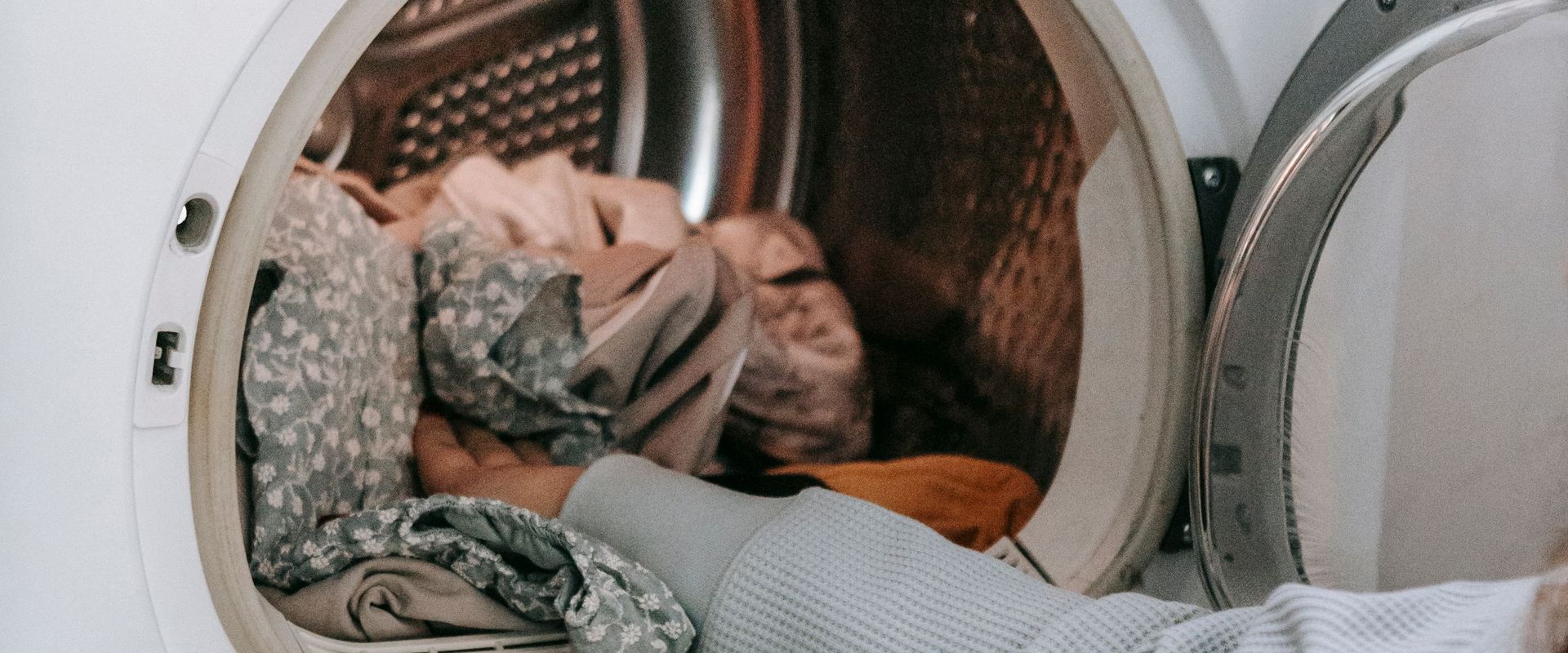 Hand loading clothes into a tumble dryer with the door open
