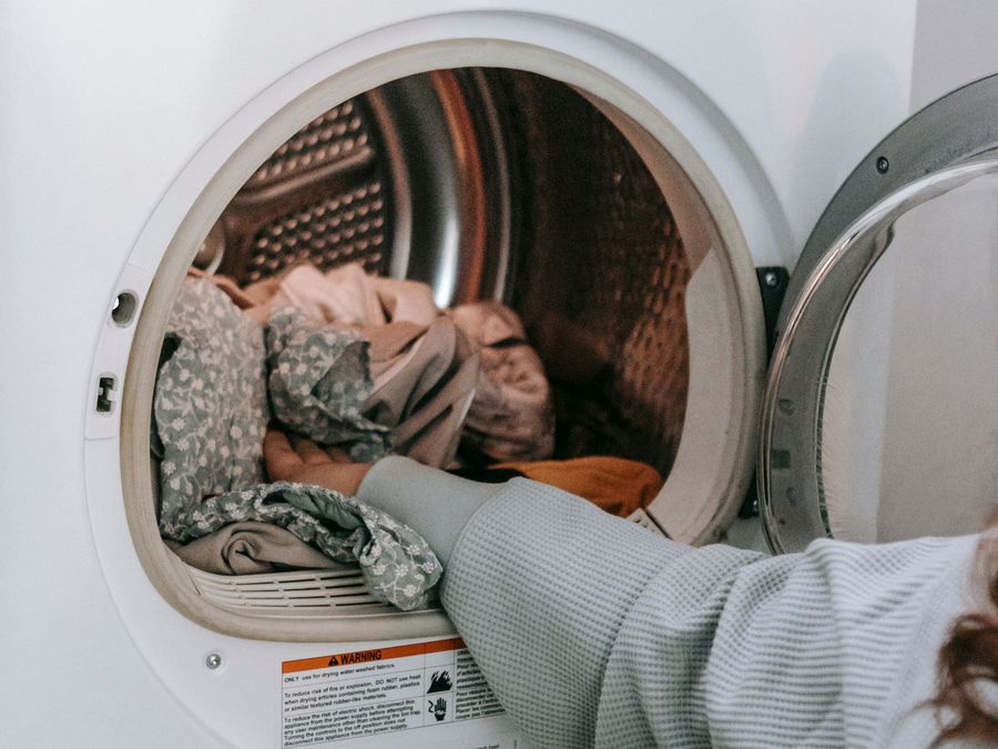 Hand loading clothes into a tumble dryer with the door open