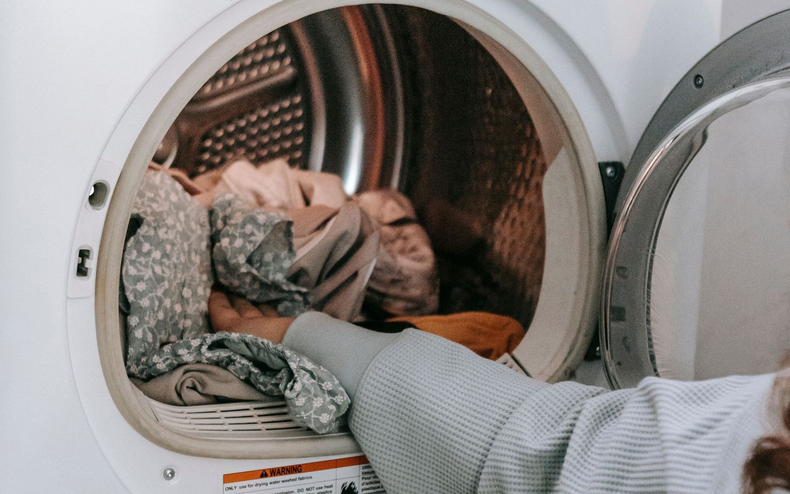 Hand loading clothes into a tumble dryer with the door open