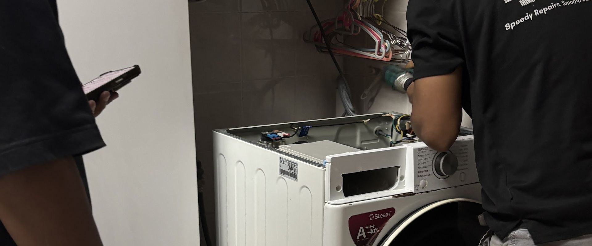 Mike's technician in a branded shirt repairing a front-load washing machine in an HDB service yard