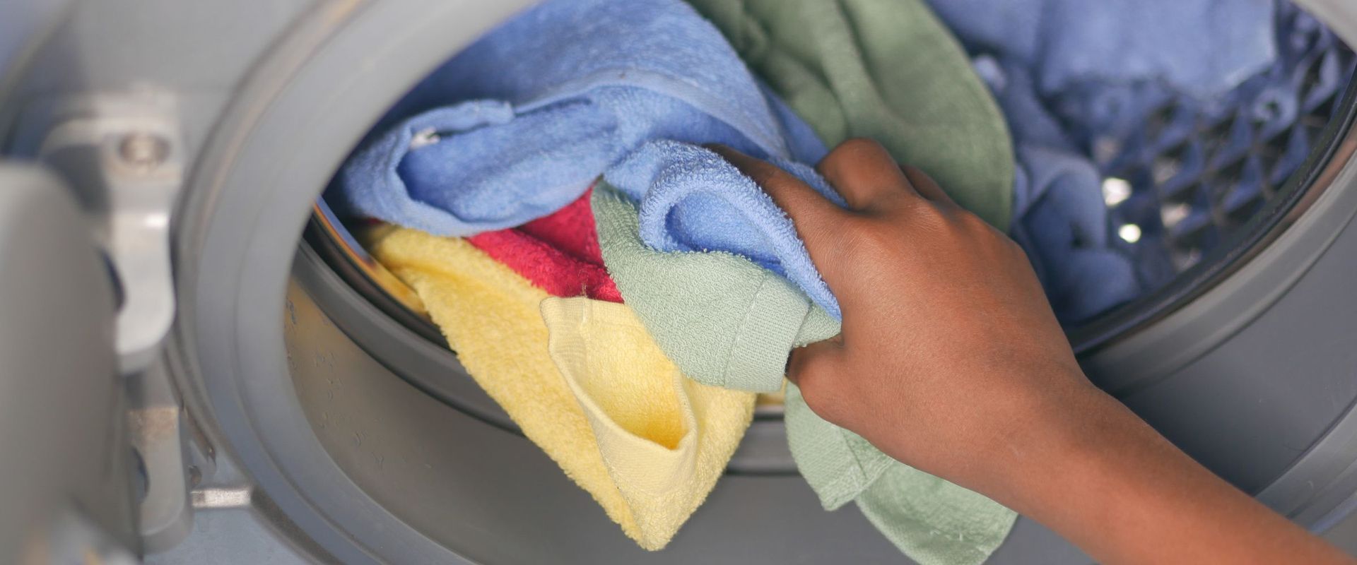 Hand loading colourful towels into a front-load washing machine