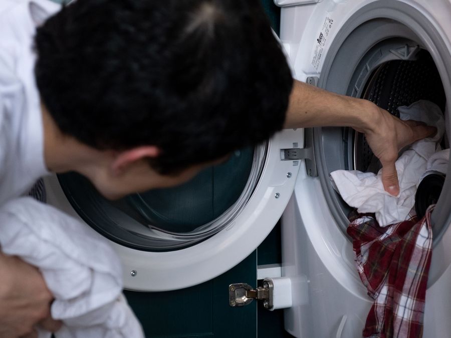 Man loading clothes into a front-load washing machine at home