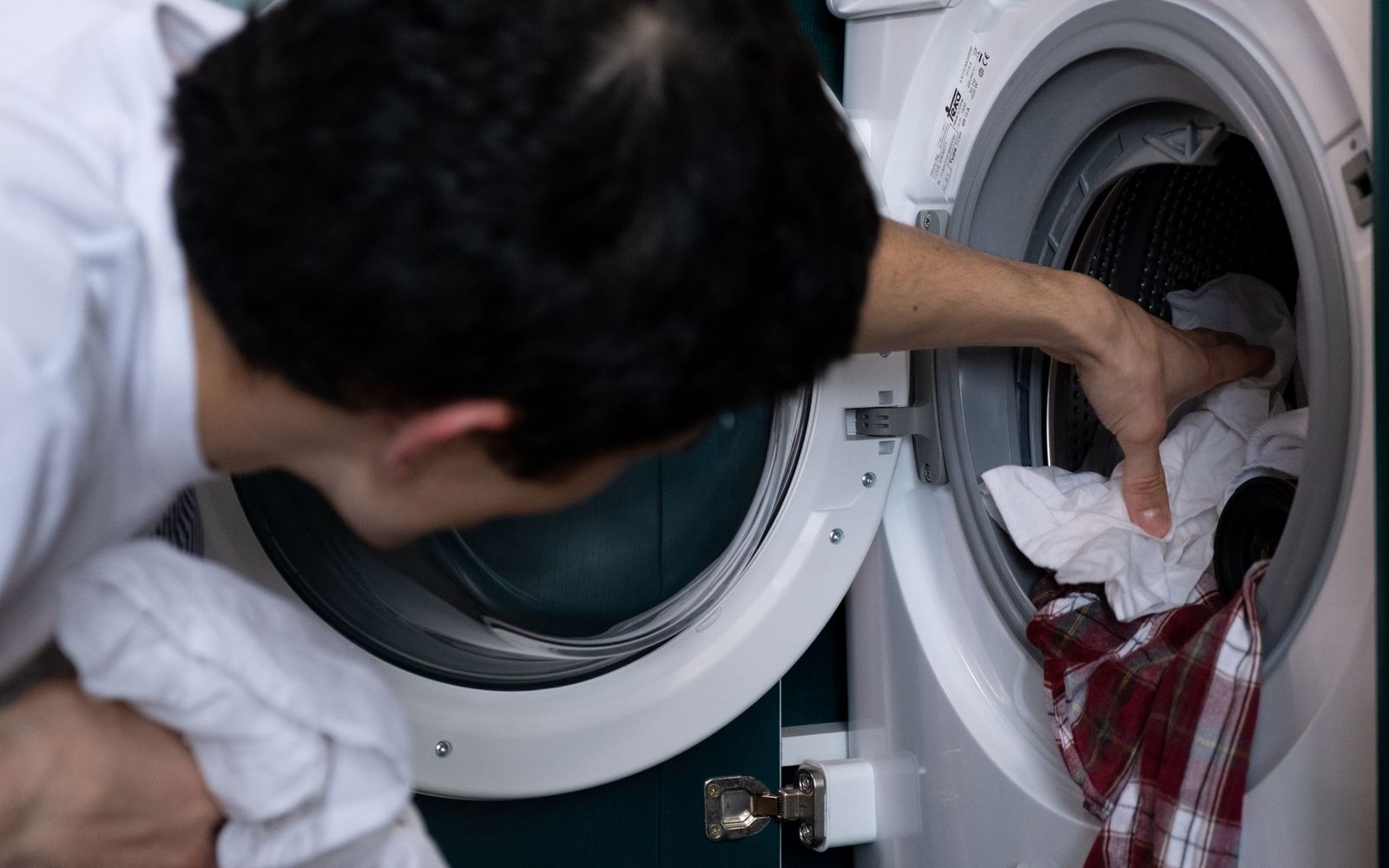 Man loading clothes into a front-load washing machine at home